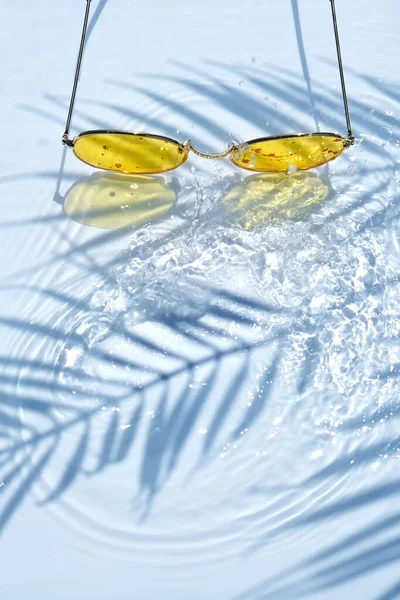 夏日平平平静静地躺着 黄色太阳镜在水的背景上 有棕榈叶的阴影和复制的空间 海滩夏季炎热天气的概念 — 图库照片