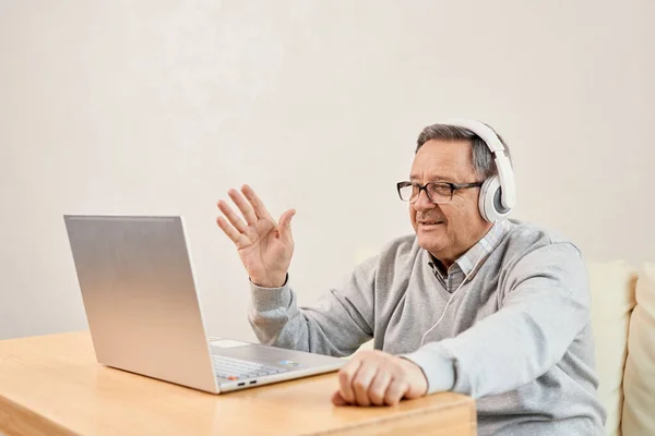 老年人在家里戴着耳机开始视频会议 成熟的男性在网上使用笔记本电脑问候治疗师 欢迎生活在国外的成年儿童 远程通信 视频会议 电子保健概念 — 图库照片