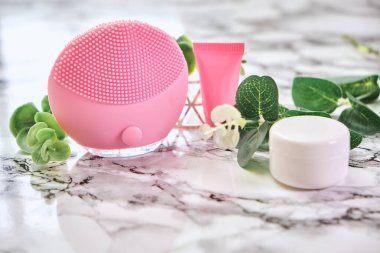 Elektrikli yüz masajı ve mermer arka planda krem. Bakım kozmetikleri ve güzellik tedavileri.