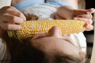 Evdeki büyük sebze mısırını ısıran kız çocuğu, taze vejetaryen yiyecekler, vitaminler, GDO 'suz sağlıklı beslenme. İç mekan. Tanınamayan yüz