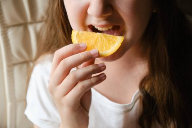 Küçük bir kız portakal dilimi yiyor, yakından, gözleri olmadan. Vitamin ve meyve.