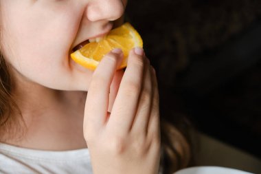 Küçük bir kız portakal dilimi yiyor, yakından, gözleri olmadan. Vitamin ve meyve.