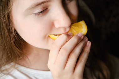 Küçük bir kız portakal dilimi yiyor, yakın plan. Vitamin ve meyve.