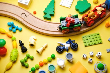 Farklı çocuk oyuncakları seti, ahşap demiryolu, tren, inşaatçı sarı arka planda metin için kopyalama alanı var. Üst görünüm