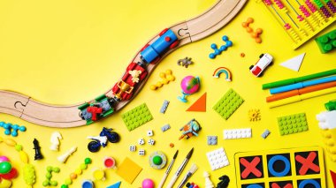 Değişik çocuk oyuncakları seti, ahşap demiryolu, tren, sarı arka planda inşaat işçisi ve metin için fotokopi alanı. Üst manzara, düz uzanma.