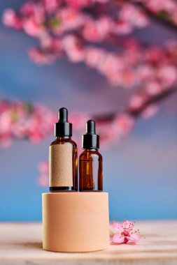Podyumda pipet ve serum olan cam şişe ve pembe gökyüzü arka planında kiraz çiçekleri dalları