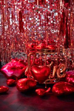 Sevgililer Günü ya da Flört için şık bir oda dekorasyonu, evlilik teklifi. Kırmızı kalp ve dudak şekilli balonlarla süslenmiş siyah duvar. Şampanya kovası, bardak ve şamdanlı bir masa.