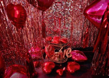 Sevgililer Günü ya da Flört için şık bir oda dekorasyonu, evlilik teklifi. Kırmızı kalp ve dudak şekilli balonlarla süslenmiş siyah duvar. Şampanya kovası, bardak ve şamdanlı bir masa.