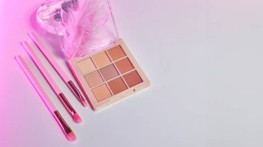 Geniş ekran arka plan dekoratif kozmetik seti beyaz bir masa, fırçalar ve göz farı. Makyaj odasındaki makyaj masasında pembe neon ışıkta dekoratif kozmetik ürünler.