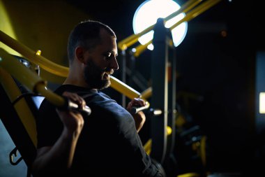 Orta yaşlı bir adam spor salonunda göğüs presi makinesinde çalışıyor, ağırlık kaldırıyor, kollarını ve gövde kaslarını geliştiriyor.
