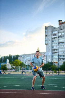Güneşli bir günde orta yaşlı bir adam şehir kortunda basketbol oynuyor. Dışarıda spor yapan güçlü bir adam. Arka planda konut binaları ve ağaçlar var. Spor, aktif yaşam tarzı konsepti