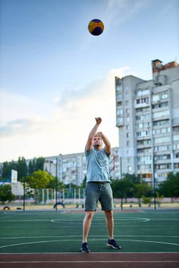 Güneşli bir günde orta yaşlı bir adam şehir kortunda basketbol oynuyor. Dışarıda spor yapan güçlü bir adam. Arka planda konut binaları ve ağaçlar var. Spor, aktif yaşam tarzı konsepti