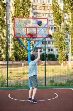 Güneşli bir günde orta yaşlı bir adam şehir kortunda basketbol oynuyor. Dışarıda spor yapan güçlü bir adam. Arka planda konut binaları ve ağaçlar var. Spor, aktif yaşam tarzı konsepti