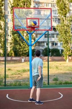 Güneşli bir günde orta yaşlı bir adam şehir kortunda basketbol oynuyor. Dışarıda spor yapan güçlü bir adam. Arka planda konut binaları ve ağaçlar var. Spor, aktif yaşam tarzı konsepti