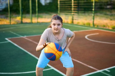 Neşeli beyaz bir kızın hayat tarzı portresi. 10 yaşında, sıcak yaz gününde basketbol topu tutuyor. Aktif yaşam tarzı, eğitim, profesyonel spor