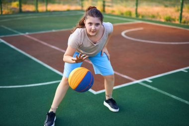 Neşeli beyaz bir kızın hayat tarzı portresi. 10 yaşında, sıcak yaz gününde basketbol topu tutuyor. Aktif yaşam tarzı, eğitim, profesyonel spor