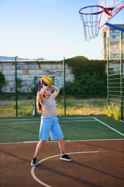 Oyun sahasında basketbol oynayan neşeli, genç bir kız. Şehir binalarının arka planında Red Court maçında şut atan bir kız. Aktif yaşam tarzı, eğitim, profesyonel spor