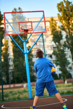 Oyun sahasında basketbol oynayan neşeli, genç bir çocuk. Çocuk şehir binalarının arka planına karşı Red Court maçında atış yapıyor. Aktif yaşam tarzı, eğitim, profesyonel spor
