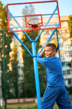 Oyun sahasında basketbol oynayan neşeli, genç bir çocuk. Çocuk şehir binalarının arka planına karşı Red Court maçında atış yapıyor. Aktif yaşam tarzı, eğitim, profesyonel spor