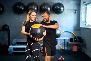 Sportif çift spor salonunda birlikte egzersiz yapıyor. Yakışıklı bir adam GYM 'de tıp topuyla egzersiz yaparken güzel bir kıza yardım ediyor..