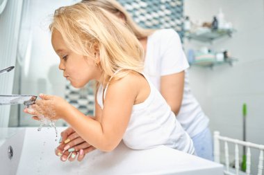 Bir anne ve çocuk sabah banyoda birlikte yüzlerini yıkıyorlar. Anne ve iki yaşındaki kızı ellerini musluk suyunun altında yıkıyorlar..