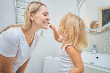 Kadın ve çocuk banyoda diş fırçasıyla birbirlerinin dişlerini fırçalıyorlar. Çocuk potansiyel olarak kendi dişlerini fırçalamayı öğreniyor. Mutlu bir aile. Diş bakımı