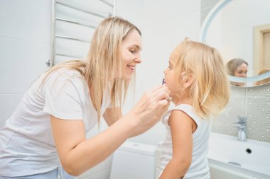 Kadın ve çocuk banyoda diş fırçasıyla birbirlerinin dişlerini fırçalıyorlar. Çocuk potansiyel olarak kendi dişlerini fırçalamayı öğreniyor. Mutlu bir aile. Diş bakımı