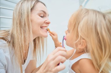 Kadın ve çocuk banyoda diş fırçasıyla birbirlerinin dişlerini fırçalıyorlar. Çocuk potansiyel olarak kendi dişlerini fırçalamayı öğreniyor. Mutlu bir aile. Diş bakımı