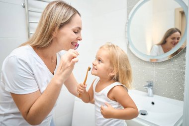 Kadın ve çocuk banyoda diş fırçasıyla birbirlerinin dişlerini fırçalıyorlar. Çocuk potansiyel olarak kendi dişlerini fırçalamayı öğreniyor. Mutlu bir aile. Diş bakımı