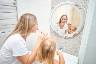 Kadın ve çocuk banyoda diş fırçasıyla birbirlerinin dişlerini fırçalıyorlar. Çocuk potansiyel olarak kendi dişlerini fırçalamayı öğreniyor. Mutlu bir aile. Diş bakımı