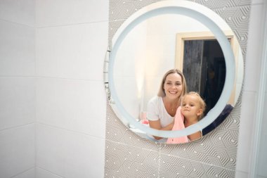 Duş, hijyen ve temiz çocuk bakımıyla bağ kurma. Bekar kadın ebeveyn evdeki banyoda sıcak bir banyo yaptıktan sonra çocuğunu yumuşak, kuru ve pembe bir havluyla kurutuyor. Aynadaki yansıma