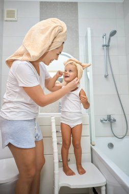 Mutlu anne, kız çocuğuna havlu takıyor. Banyoda küçük tatlı bir kızı olan genç bir anne. Sağlık ve aile kavramı. Evdeki neşeli güzellik günü.