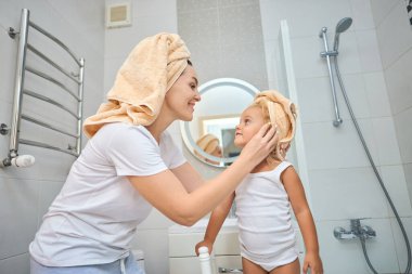 Mutlu anne, kız çocuğuna havlu takıyor. Banyoda küçük tatlı bir kızı olan genç bir anne. Sağlık ve aile kavramı. Evdeki neşeli güzellik günü.