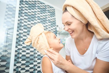 Mutlu anne, kız çocuğuna havlu takıyor. Banyoda küçük tatlı bir kızı olan genç bir anne. Sağlık ve aile kavramı. Evdeki neşeli güzellik günü.