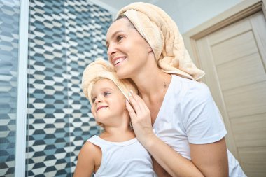 Anne ve küçük kızın başları havluyla örtülü ve beyaz bezle banyoda mutlulukla dalga geçişlerini yakından çek. Sağlık ve rahatlama ve aile ilişkileri hakkında fikir.