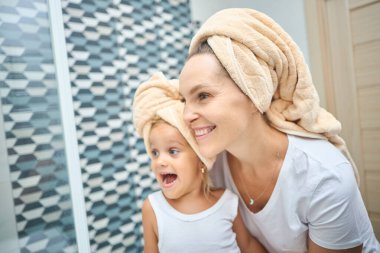 Anne ve küçük kızın başları havluyla örtülü ve beyaz bezle banyoda mutlulukla dalga geçişlerini yakından çek. Sağlık ve rahatlama ve aile ilişkileri hakkında fikir.