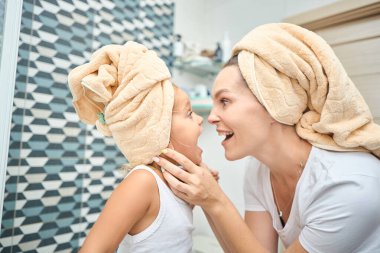 Anne ve küçük kızın başları havluyla örtülü ve beyaz bezle banyoda mutlulukla dalga geçişlerini yakından çek. Sağlık ve rahatlama ve aile ilişkileri hakkında fikir.