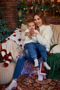 Mutlu anne ve küçük çocuk Noel tatili boyunca evde rahat vakit geçirirken Noel ağacının yanındaki kanepede birlikte oturuyorlar. Kapalı etkinlikler.