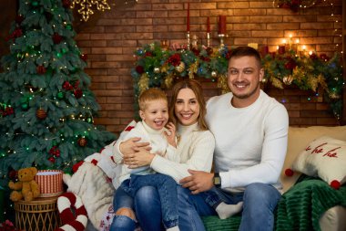 Mutlu aile Noel ağacının yanında sımsıkı sarılıyor ve güzel bir evde Noel arifesinde neşeyle gülümsüyor.