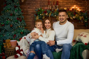 Mutlu aile Noel ağacının yanında sımsıkı sarılıyor ve güzel bir evde Noel arifesinde neşeyle gülümsüyor.