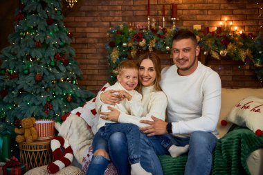 Mutlu aile Noel ağacının yanında sımsıkı sarılıyor ve güzel bir evde Noel arifesinde neşeyle gülümsüyor.