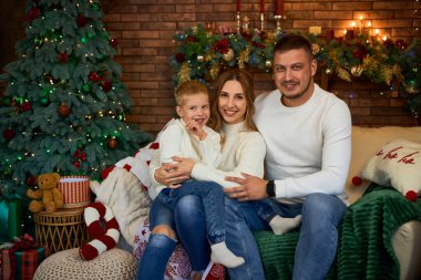 Mutlu aile Noel ağacının yanında sımsıkı sarılıyor ve güzel bir evde Noel arifesinde neşeyle gülümsüyor.