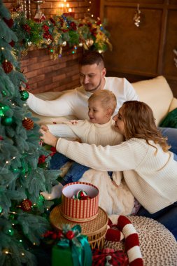 Mutlu aile Noel ağacını süslüyor ve güzel bir evde Noel arifesinde neşeyle gülümsüyor.