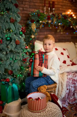 Noel ağacının yanında hediye kutusuna sarılan tatlı çocuk. Mucizeler ve tatil bekleyen bir çocuk.