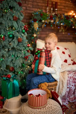 Noel ağacının yanında hediye kutusuna sarılan tatlı çocuk. Mucizeler ve tatil bekleyen bir çocuk.