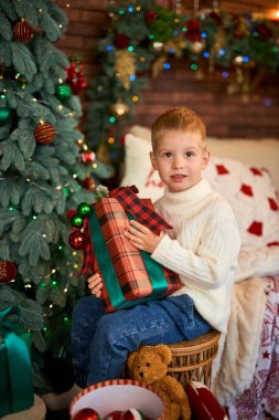 Noel ağacının yanında hediye kutusuna sarılan tatlı çocuk. Mucizeler ve tatil bekleyen bir çocuk.