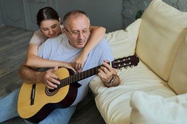 Çocuk gitar çalarken dedesine sarılıyor. Birlikte vakit geçirmek, aile, yaşlılık.