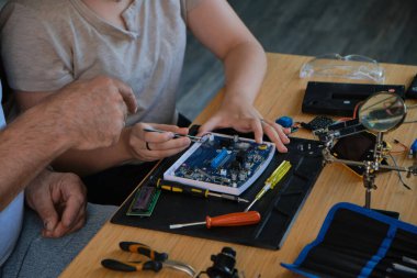 Büyükbaba torununa evde elektronik aletlerin nasıl tamir edileceğini öğretiyor, öğrenme ve beceri geliştirmeyi teşvik ediyor. Eğitim, aile ve DIY tamir temaları için ideal