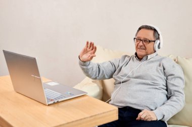 Evdeki bilgisayarında video görüşmesi sırasında kulaklık sallayan son sınıf öğrencisi. Çevrimiçi iletişim, yaşlılar için teknoloji ve uzak bağlantı temaları için ideal