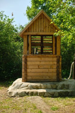 İçinde bir kova olan rustik ahşap su kuyusu, parlak yeşil yapraklar ve güneşli bir günde ağaçlarla çevrili taş basamaklarda duruyor. Kırsal yaşam ve doğal kaynaklar kavramı